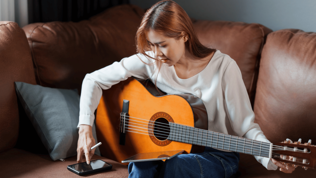 Young person practicing guitar with an app on their phone