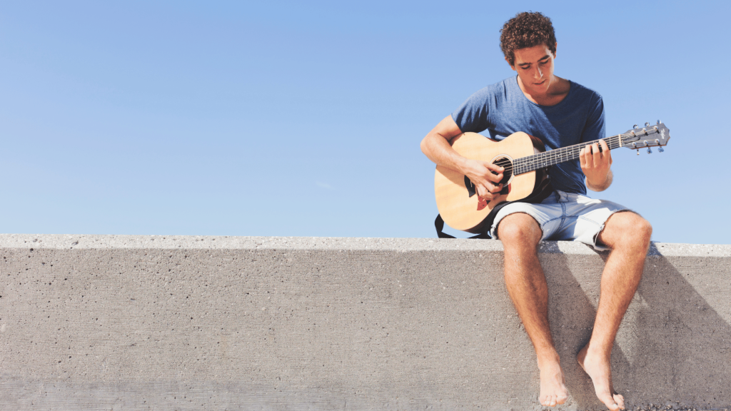 Young person outdoors playing an acoustic guitar